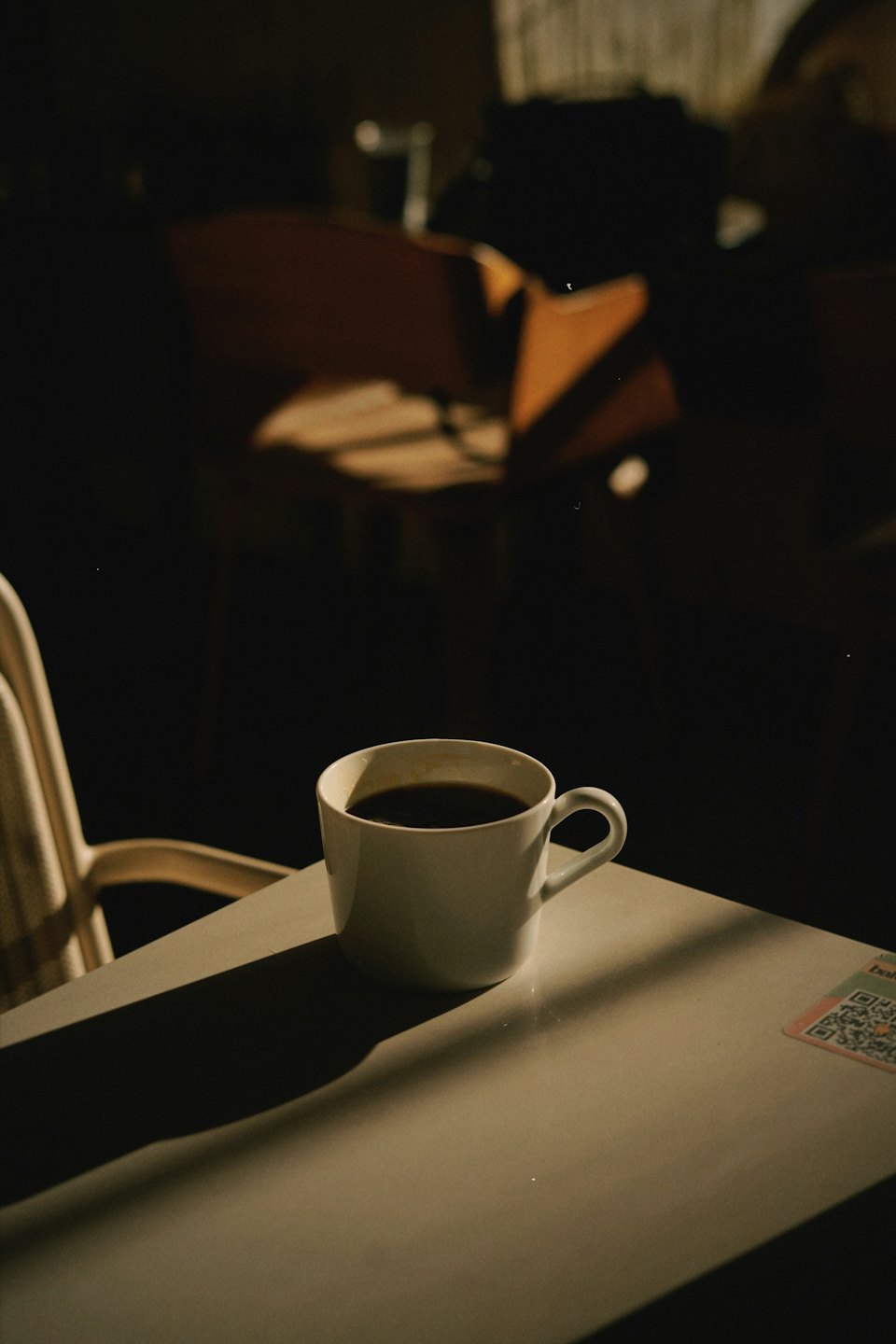 Dark coffee in a white mug sits on a cafe table.