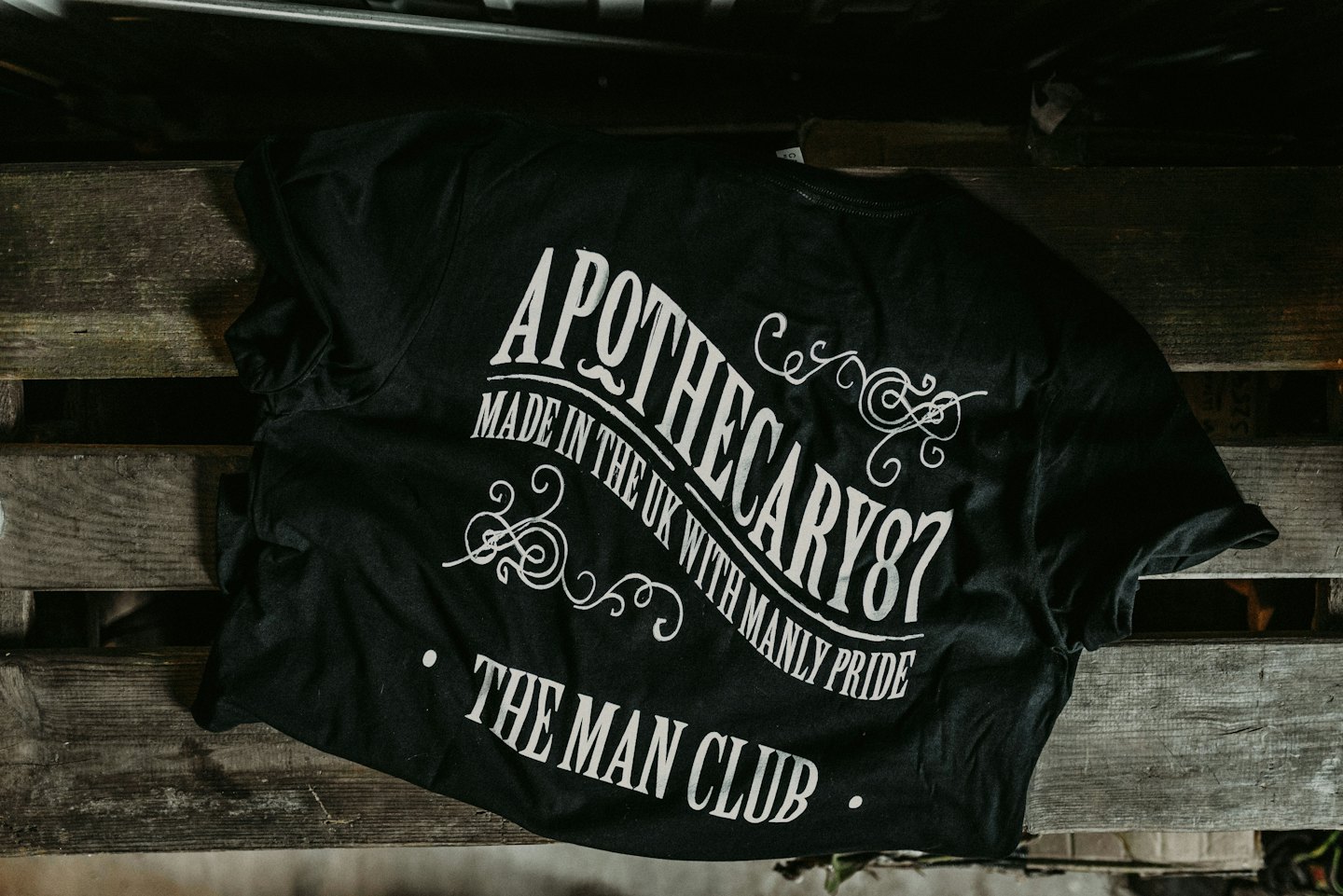 Black t-shirt with white vintage design resting on wooden pallet.